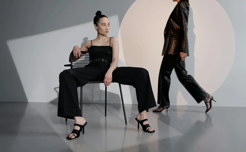 Model sitting down on chair in black attire with another model walking behind