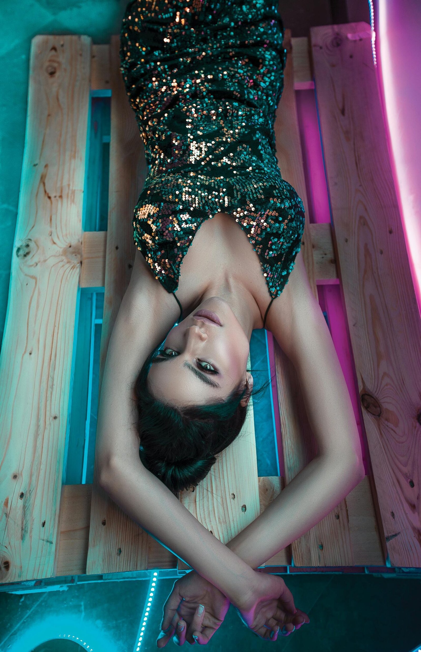 Seductive model in glittery dress next to neon lights laying down